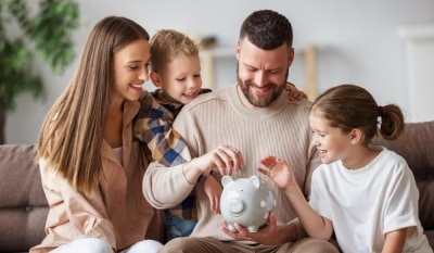 Smiling parents and two children sitting together putting money in a piggy-bank